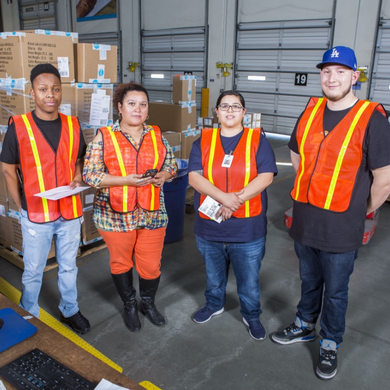 Four warehouse workers in orange hi-vis vests